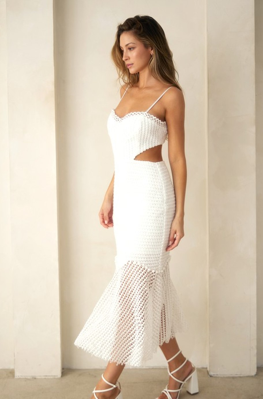 The Sorrento Dress in white, side view - fitted crochet midi with fluted sheer net hem